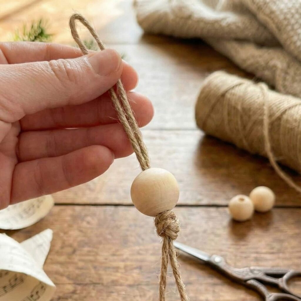 Výroba DIY dekorace anděla - výroba hlavičky z korálku a provázku na rustikálním dřevěném stole.