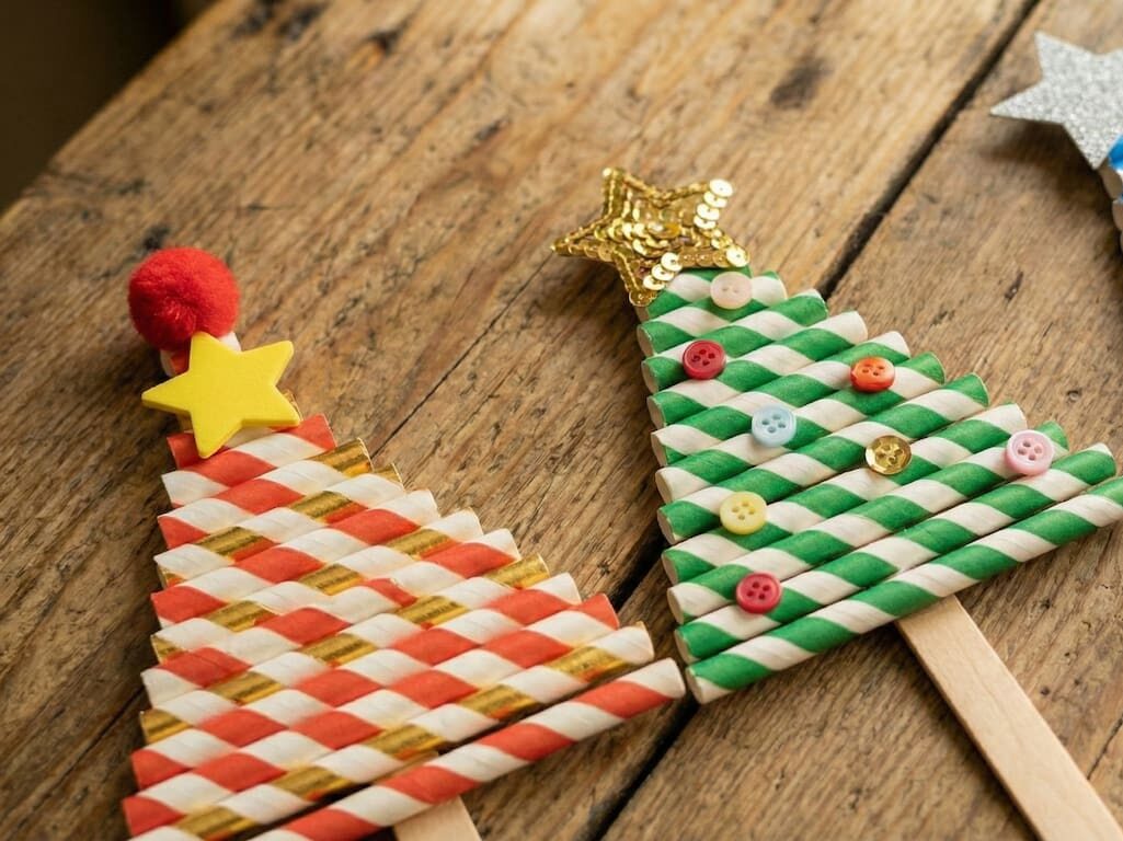 Tři různé varianty hotových vánočních stromečků z brček na stole. Vlevo červeno-zlatý s bambulkou a hvězdou, uprostřed zeleno-bílý s knoflíky a zlatou hvězdou, vpravo modro-stříbrný se stříbrnou hvězdou a vločkami.