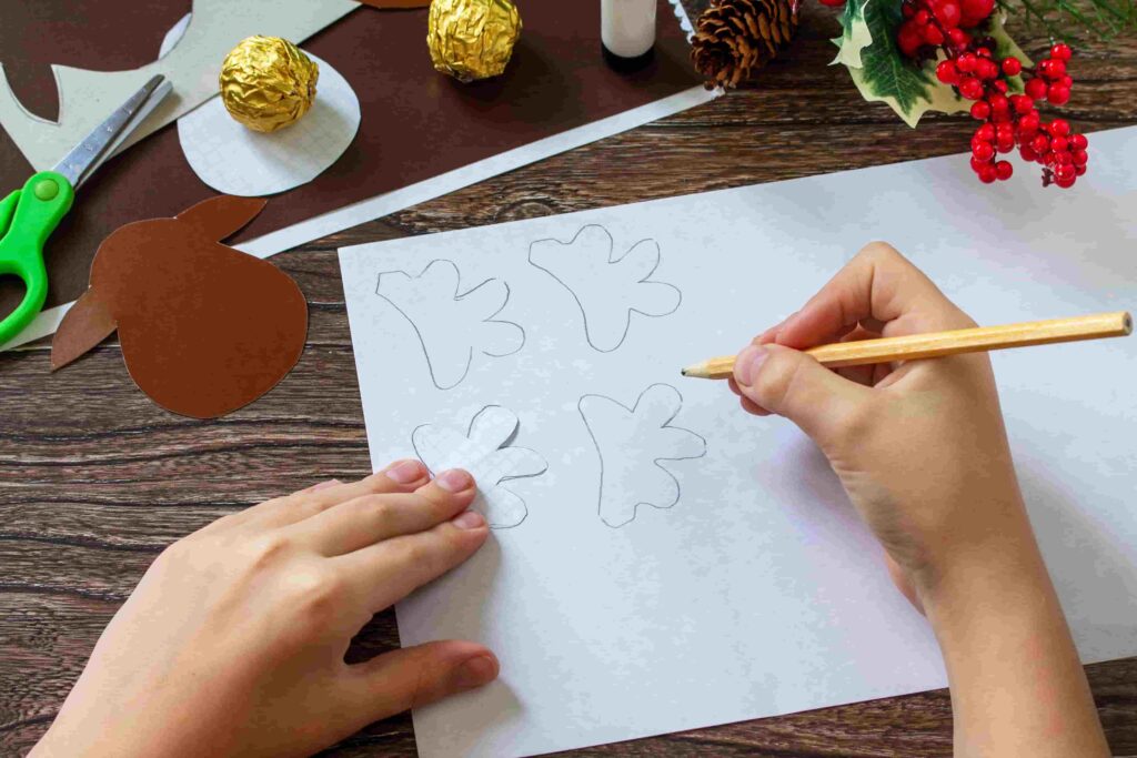 Dítě kreslí tužkou na bílý papír obrysy sobích parohů, vedle leží již vystřižená šablona.