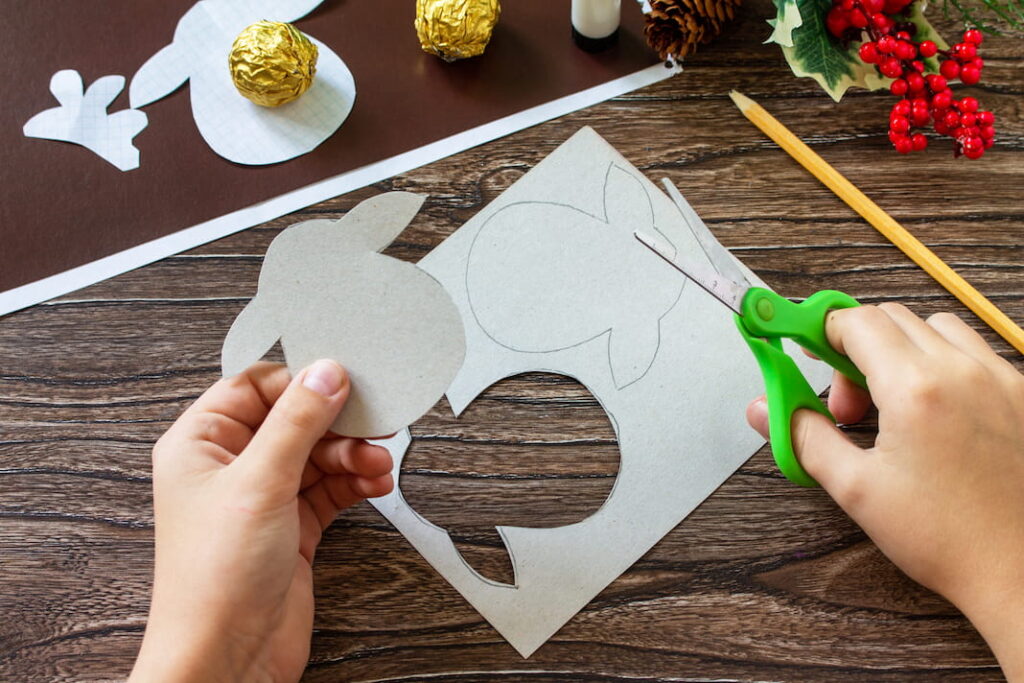 Dítě nůžkami vystřihuje z kartonu tvar hlavy soba. V kartonu je již vystřižený otvor.