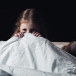 Vystrašené dítě, které se bojí bubáků se schovává pod peřinou.