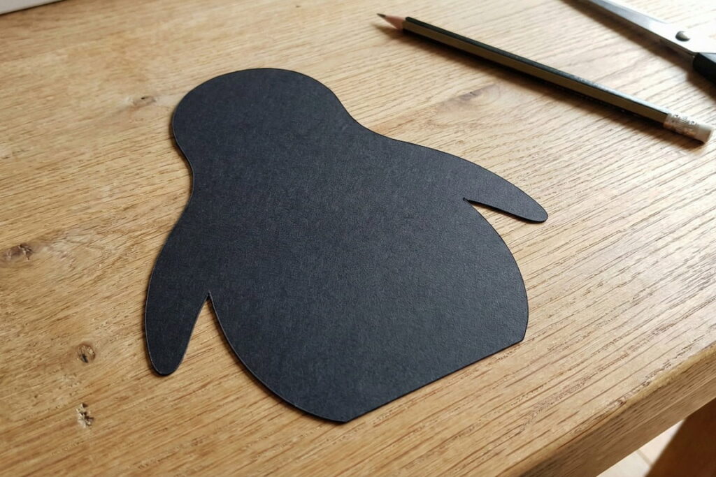 Černý papírový výstřižek těla tučňáka na dřevěném stole.