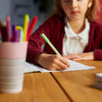 Školačka sedící u stolu píše domácí úkoly.
