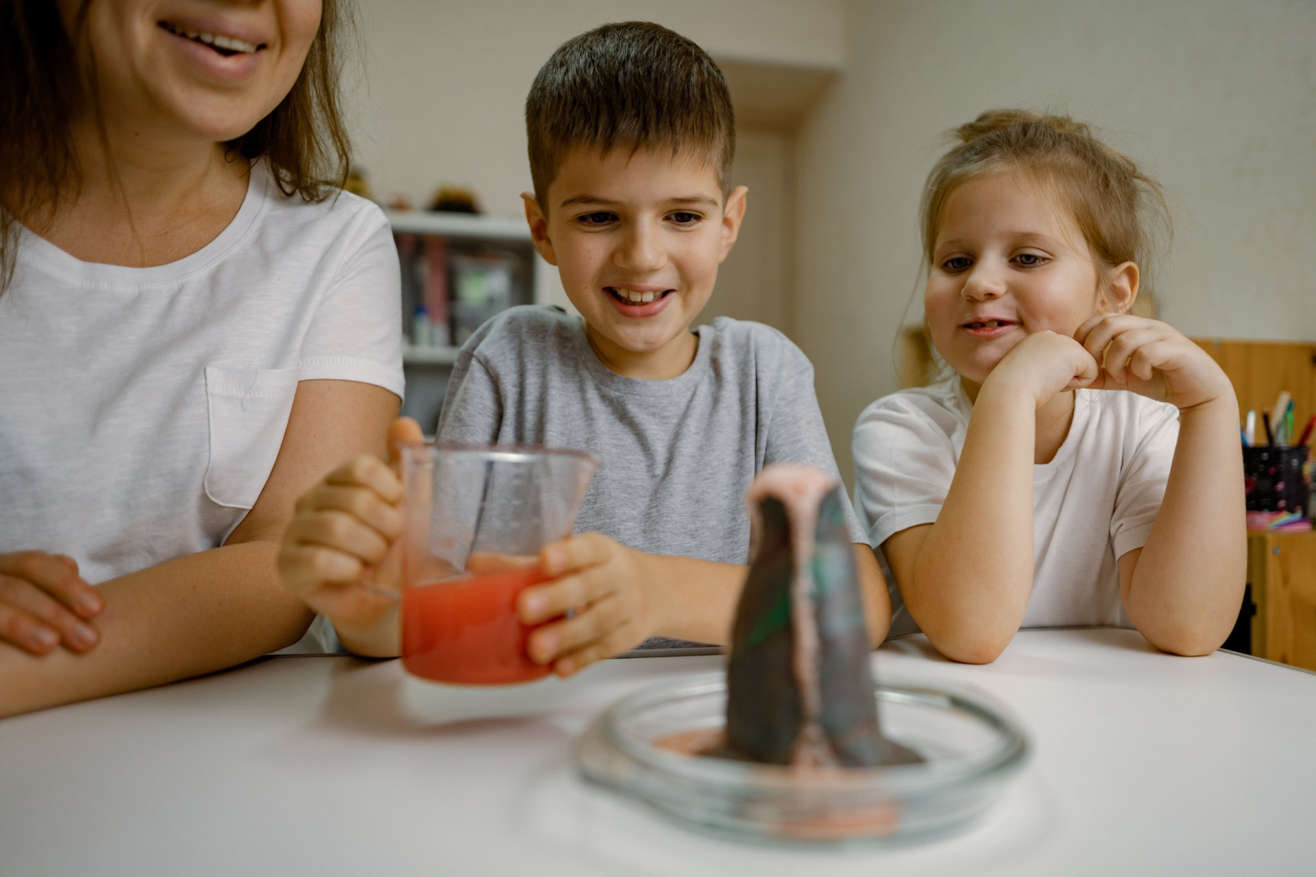Maminka a dvě děti u modelu domácí sopky s obarvenou tekutinou.